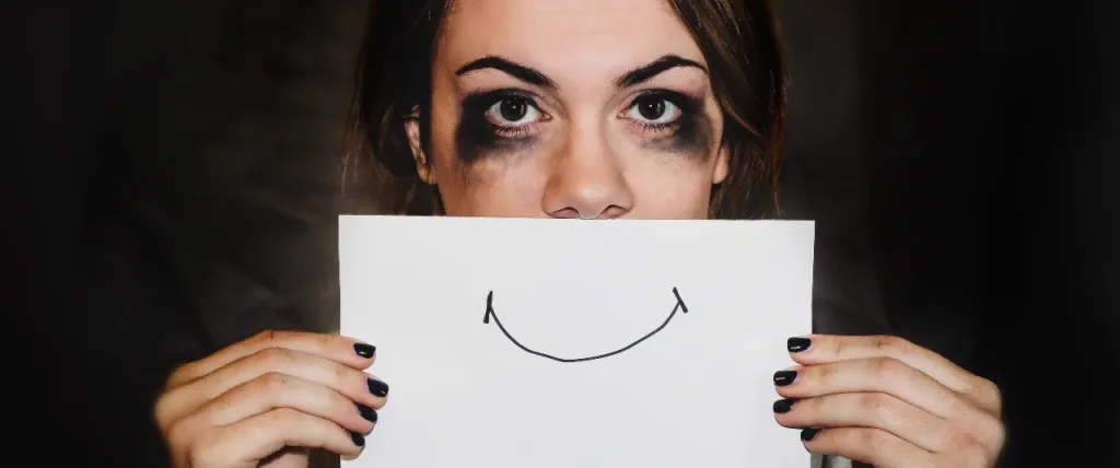 Person crying but holding piece of paper over their mouth with a smile drawn on it