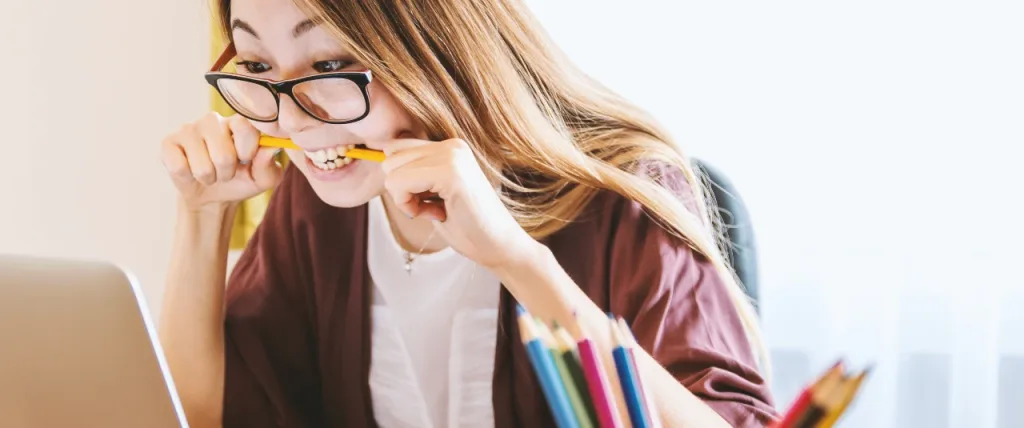 Frustrated employee bites down on pencil whilst looking at their laptop screen.