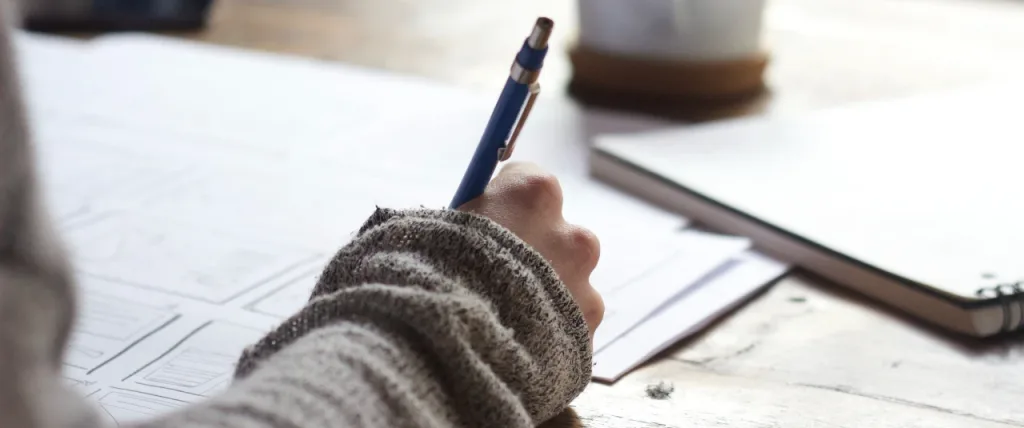 Person holding a pen writting whilst sat at a desk