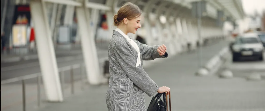 Woman looking at watch whilst standing with her suitcase.